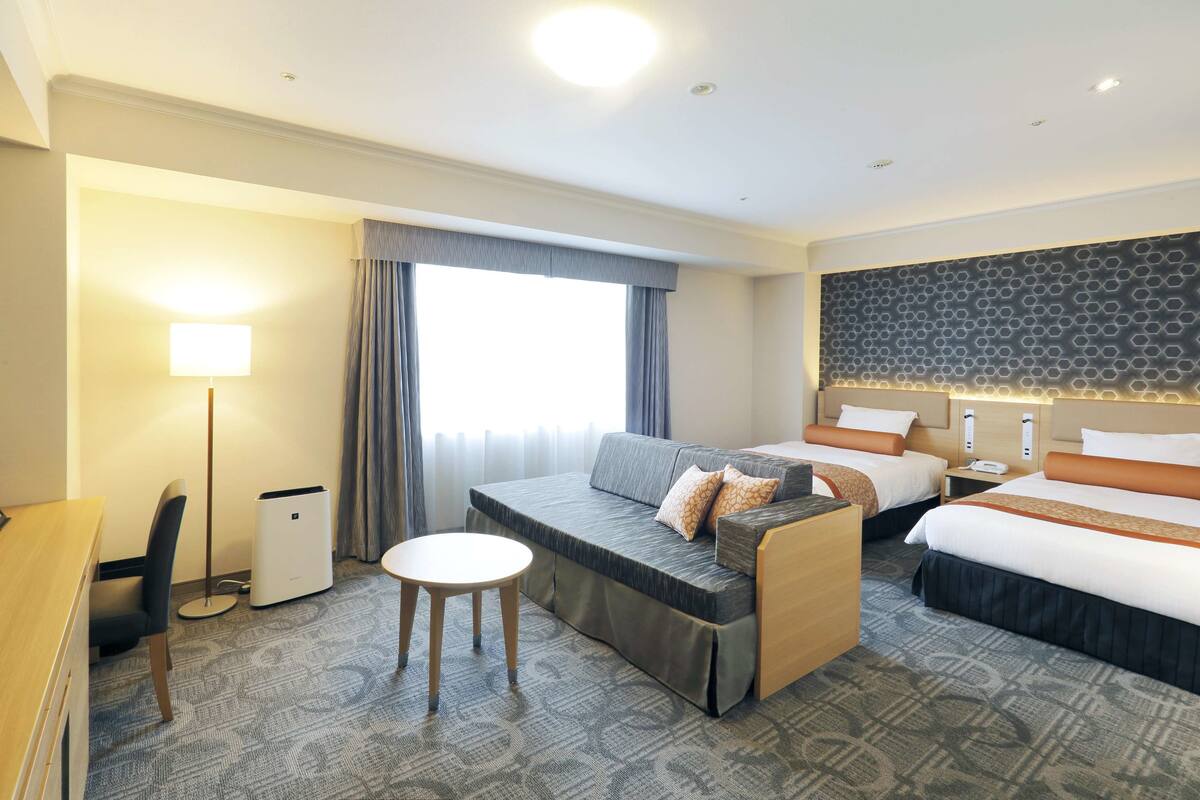 Ein Hotelzimmer mit einer Couch, zwei Betten, einem Schreibtisch und einer Lampe.