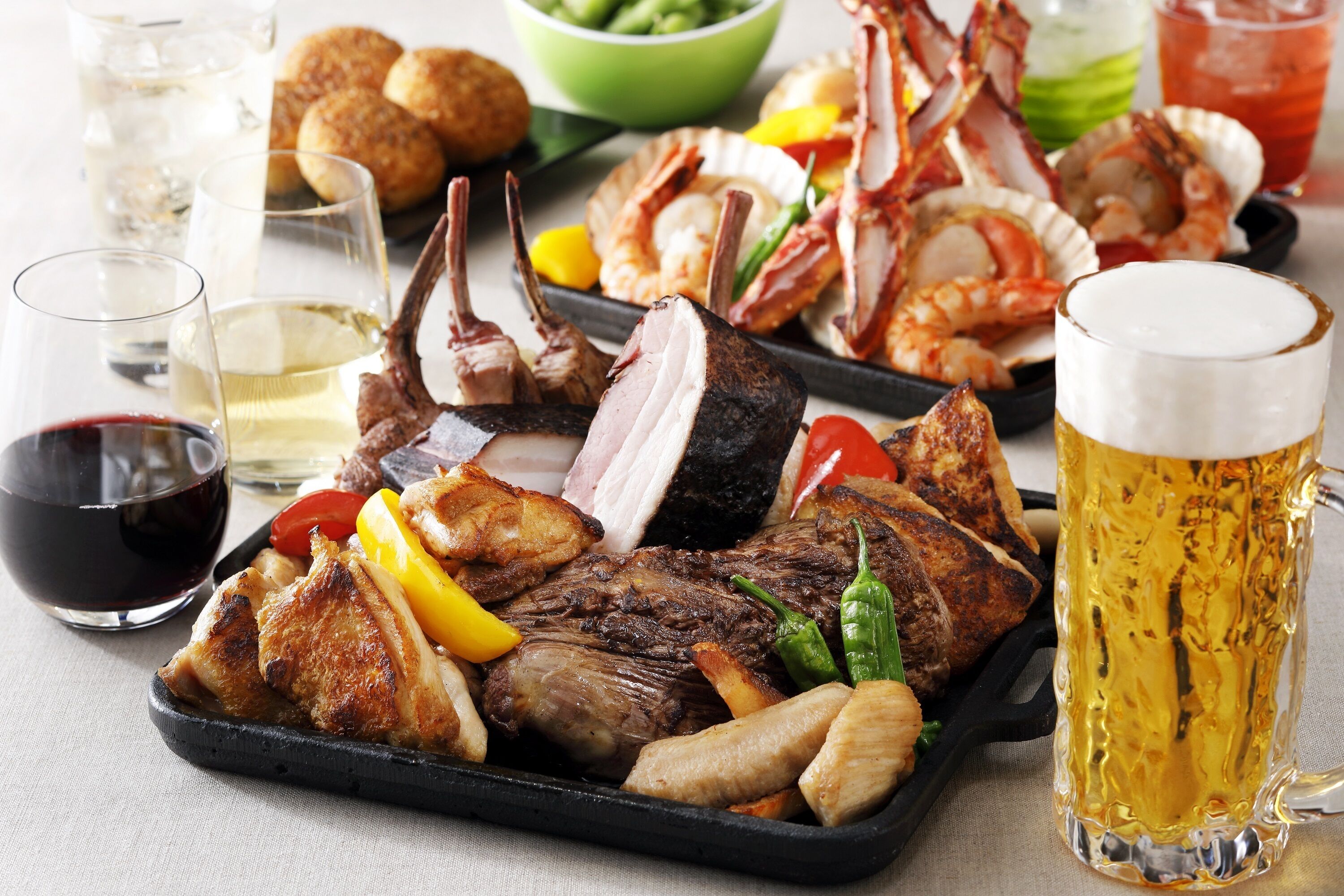 Diversos tipos de carnes grelhadas e frutos do mar dispostos numa bandeja, acompanhados por um copo de cerveja e taças de vinho.