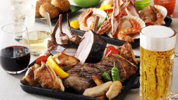 Diversos tipos de carnes grelhadas e frutos do mar dispostos numa bandeja, acompanhados por um copo de cerveja e taças de vinho.
