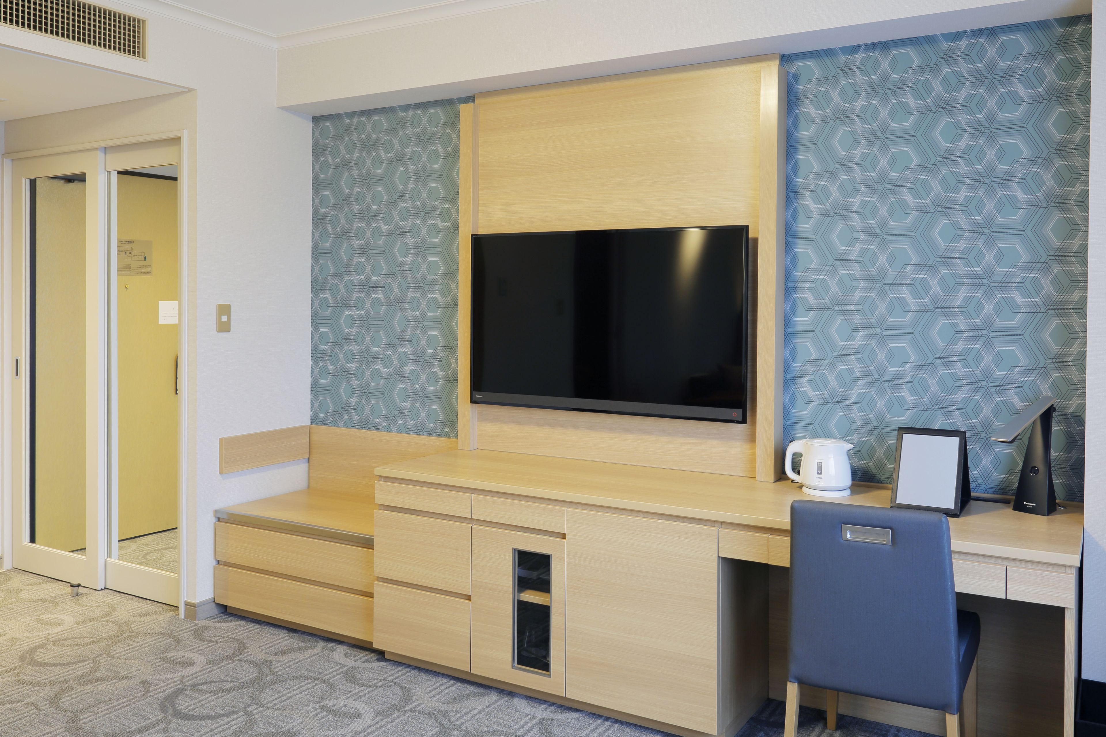 Quarto de hotel com escrivaninha de madeira, televisão de tela plana, cafeteira e uma cadeira.