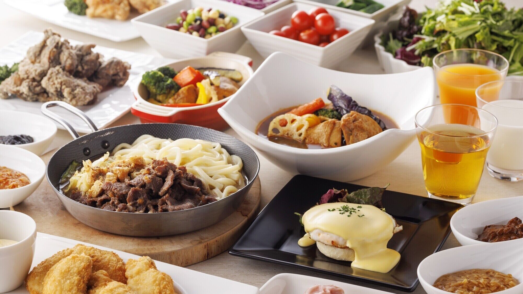 A variety of dishes including a pan with noodles and meat, a plate with a poached egg, and several side dishes in bowls.