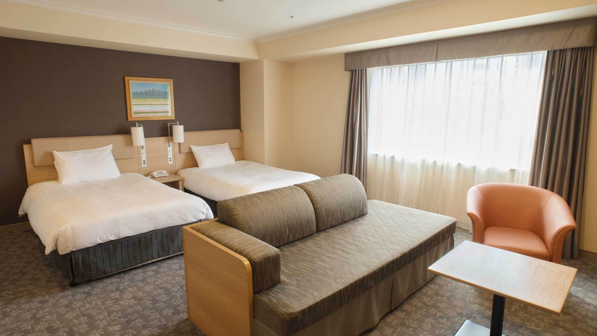 A hotel room with two beds, a sofa, a chair, a small table, and a painting on the wall.