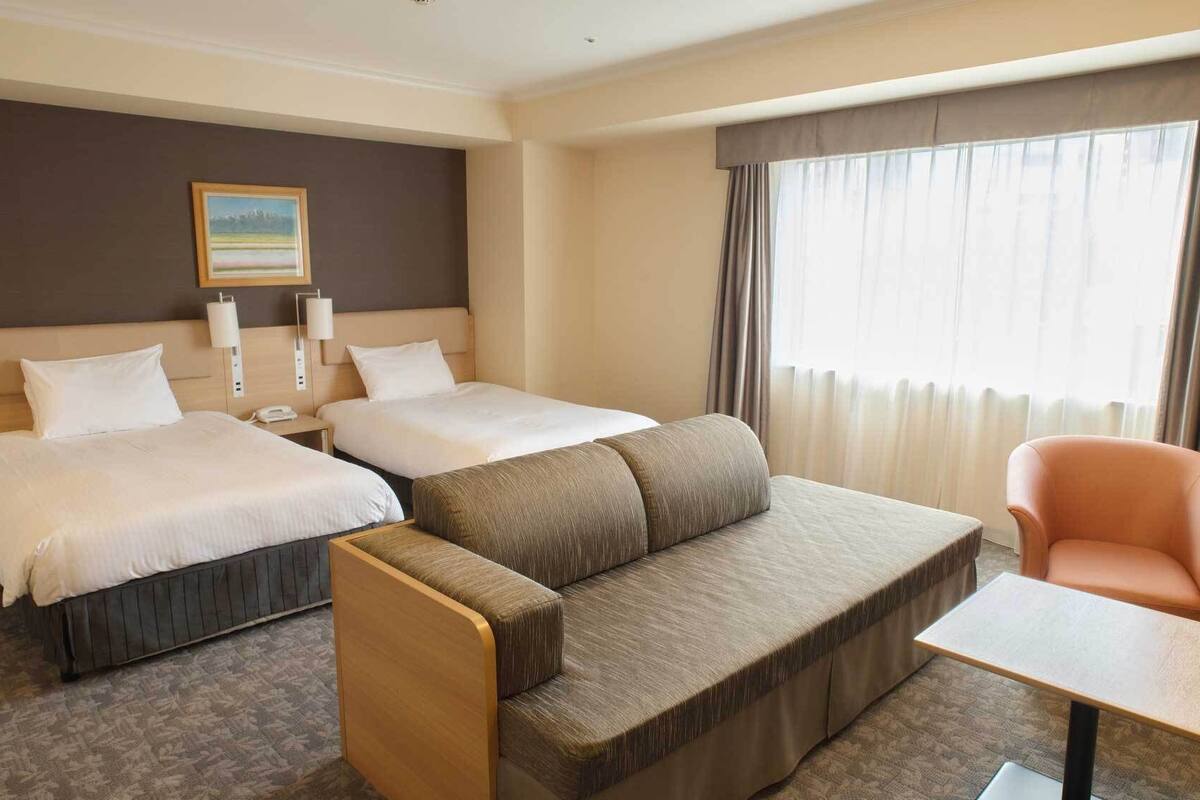 Ein Hotelzimmer mit zwei Betten, einer Couch, einem Sessel, einem kleinen Tisch und einem Bild an der Wand.
