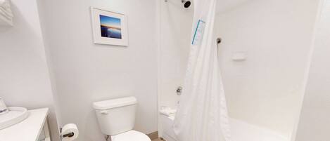 A bathroom with a toilet, a shower, and a small framed picture on the wall.