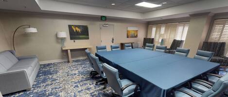 A conference room with a large table, six chairs, a sofa, and a patterned carpet.