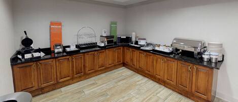 A breakfast bar with a waffle maker, coffee machine, and a sign for indulgent spread sprinkle.