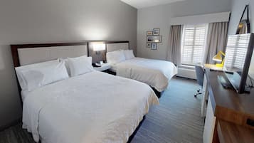 Een hotelkamer met twee bedden, een bureau met stoel, een bureaulamp, een flatscreen televisie en een raam met gordijnen.