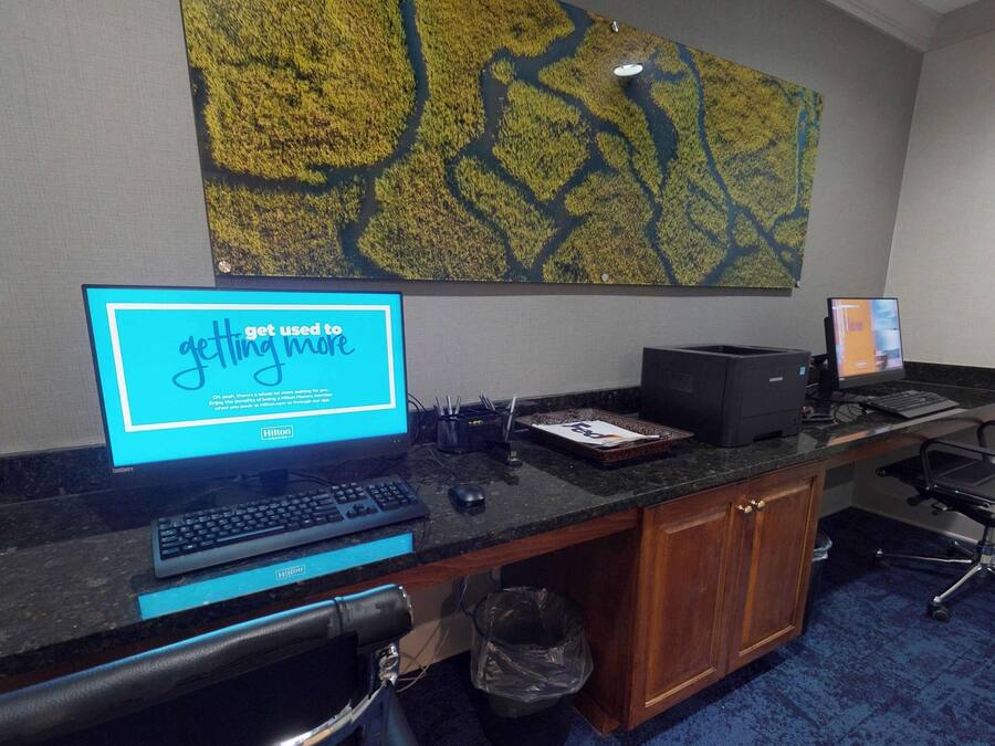 Un mostrador de recepción de hotel con una computadora, una impresora y un cubo de basura.