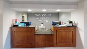 A reception desk with a "Welcome to the Peach State" sign, two computer monitors, a plant, and a Hilton sign. - Hampton Inn St. Simons Island (St. Simons Island)