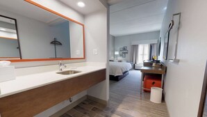 A hotel bathroom with a large mirror, sink, and a shower area. - Hampton Inn St. Simons Island (St. Simons Island)