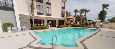 A pool area with a clear blue pool, surrounded by lounge chairs and palm trees.