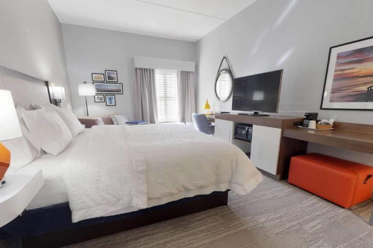 A modern hotel room with a large bed, a desk, a TV, and a window with curtains.