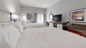 A hotel room with two beds, a desk with a television, a chair, and a window with curtains.