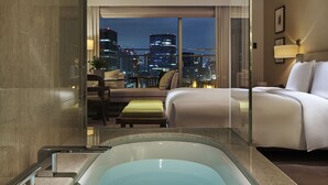 Une chambre d’hôtel avec une grande baignoire, un lit, un canapé et une vue sur la ville.