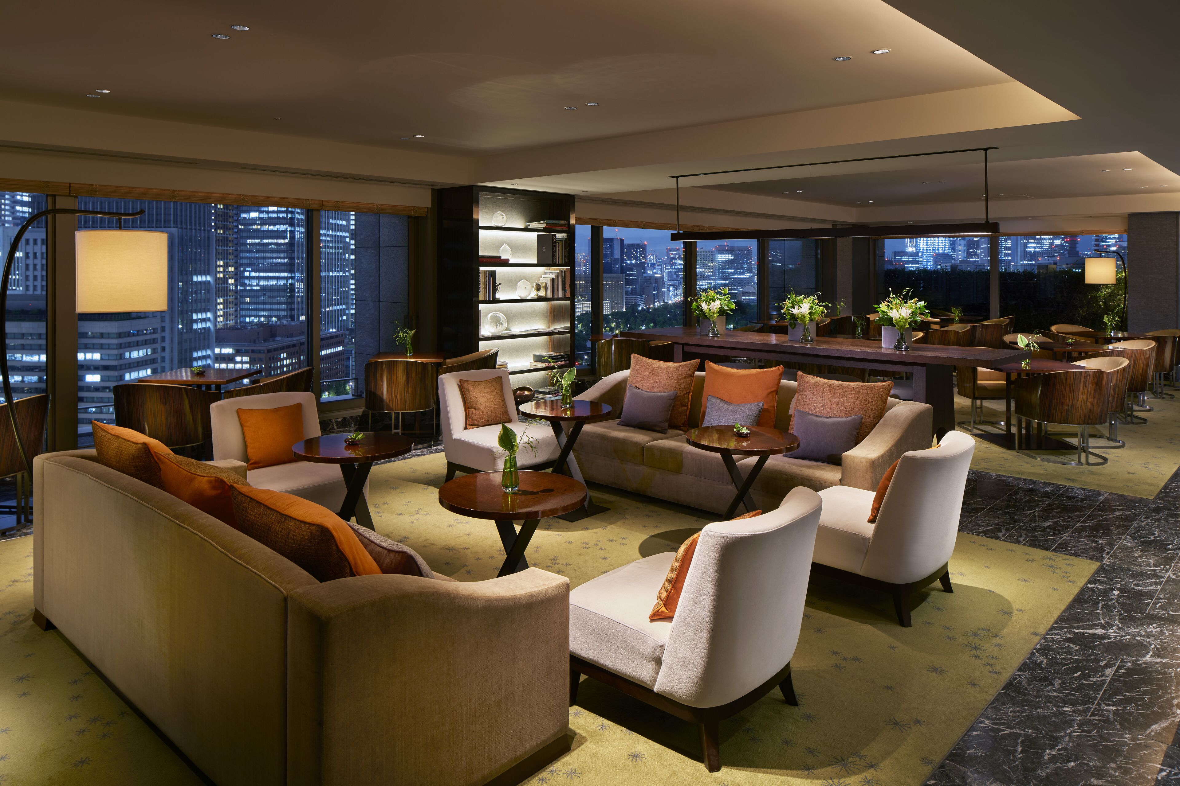 A modern living room with sofas, armchairs, and a coffee table, featuring a city view through large windows.