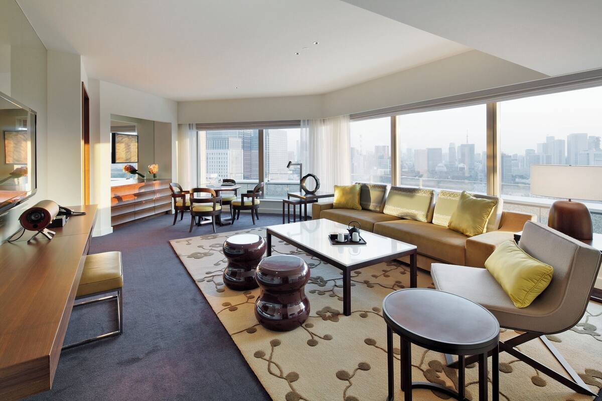 A spacious living room with a sofa, coffee table, and seating area, large windows with a city view, and a modern design.