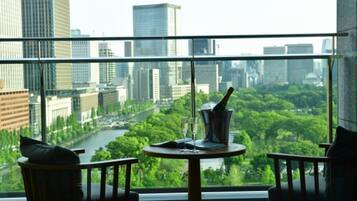A room with a view of a cityscape and a river, featuring a table with a bottle and glasses.