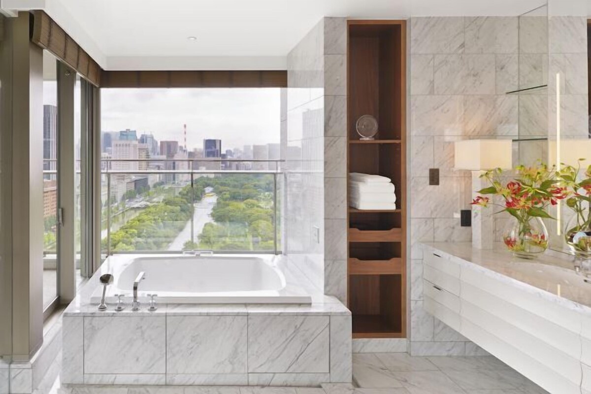 A modern bathroom with a large bathtub, a glass-enclosed shower, and a view of a cityscape.