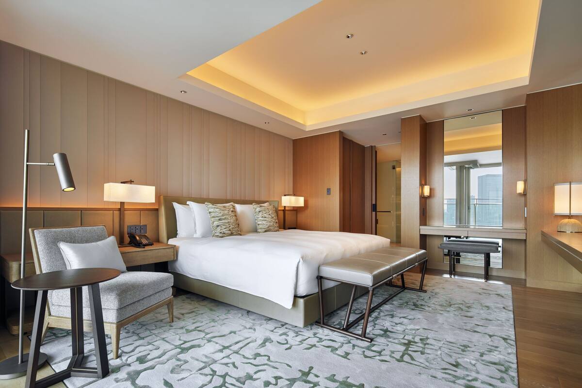 A modern hotel room with a large bed, a desk, a chair, and a small table.