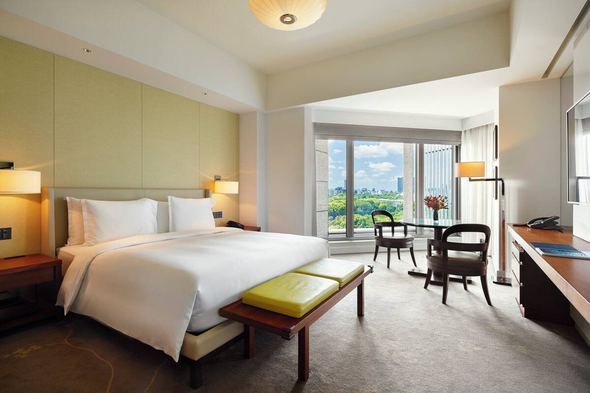 A hotel room with a large bed, a desk, a chair, and a view of the outdoors.