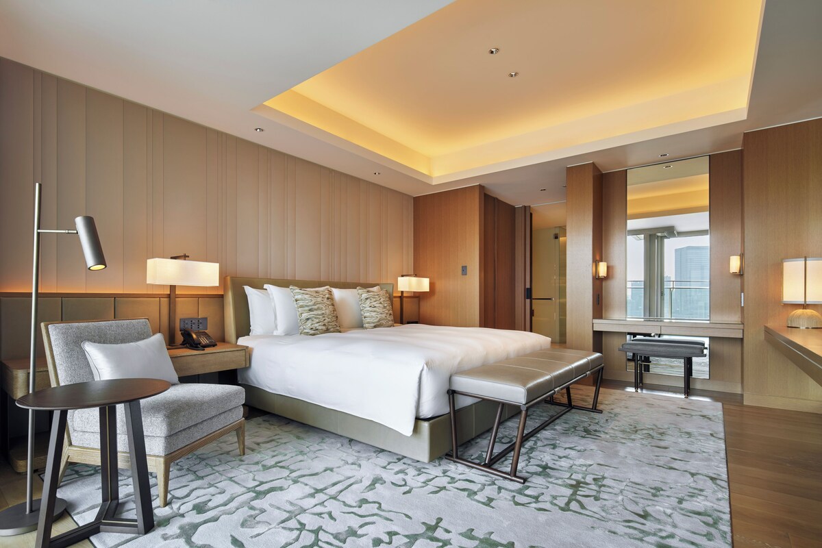 A hotel room with a bed, bedside tables, a desk, a chair, and a large mirror.