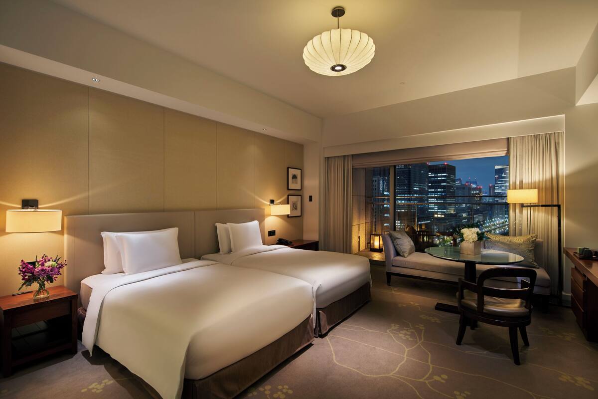 A hotel room with two beds, a sofa, a dining table, and a city view.