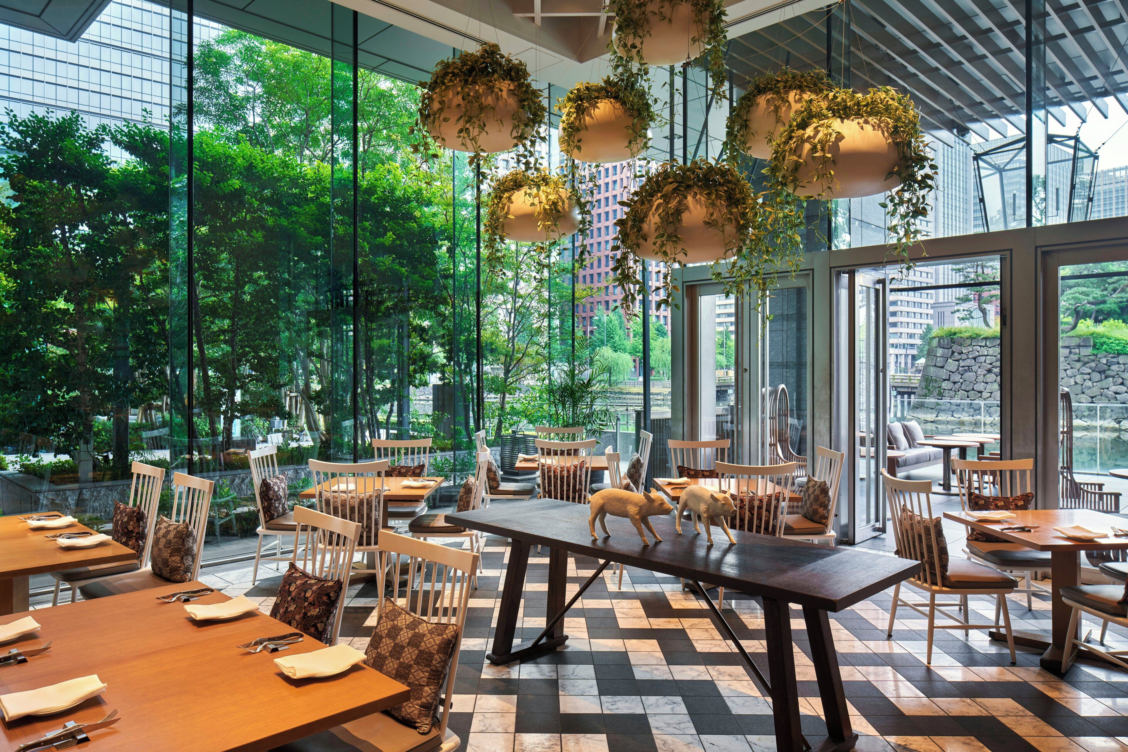 A restaurant with large windows, wooden tables, and hanging plants.