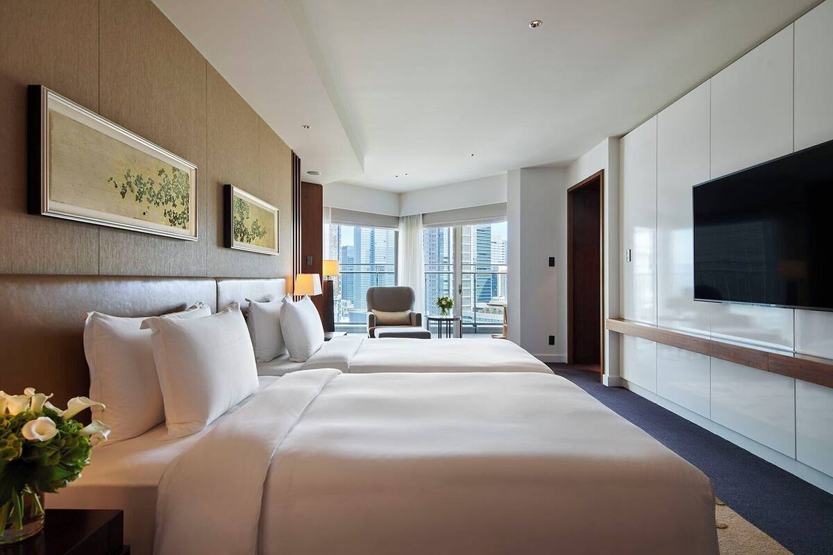 A hotel room with two beds, a TV, and a view of the city.