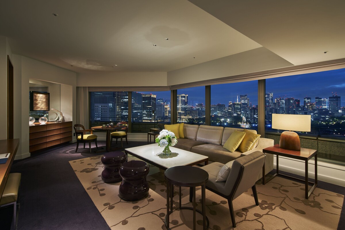 A modern living room with a city view, a sofa, a coffee table, and a dining area.