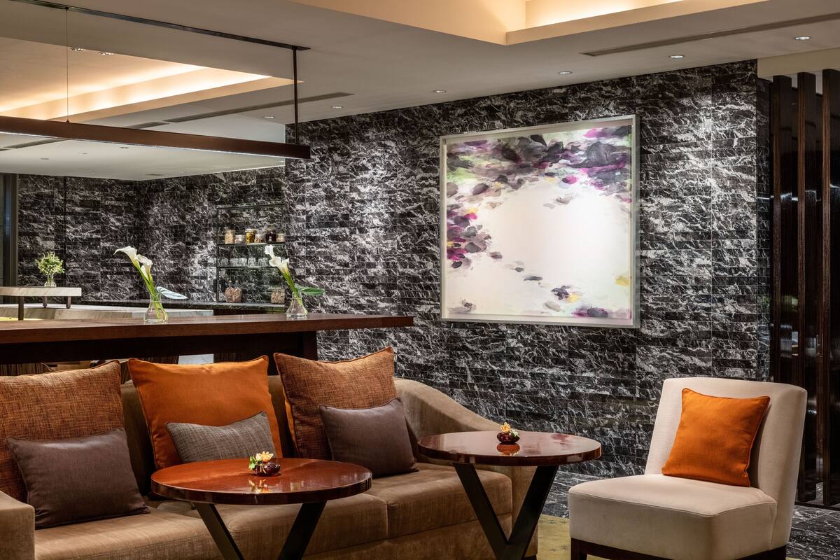 A modern lobby with a marble wall, a large abstract painting, and a seating area with sofas and tables.