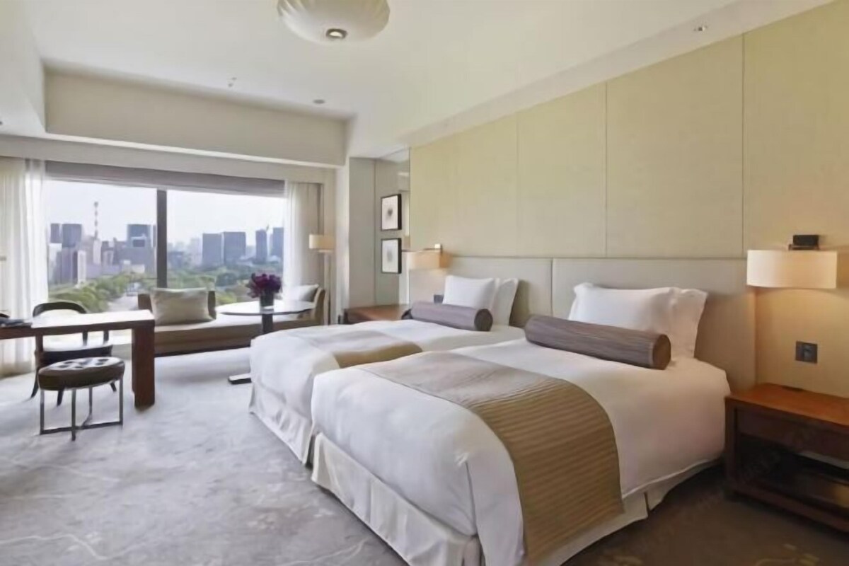 A hotel room with two beds, a desk, and a view of the city.