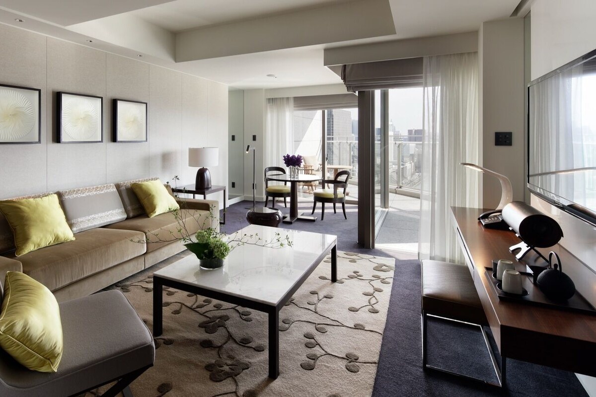 A modern hotel room with a sofa, coffee table, and a dining area with a table and chairs.