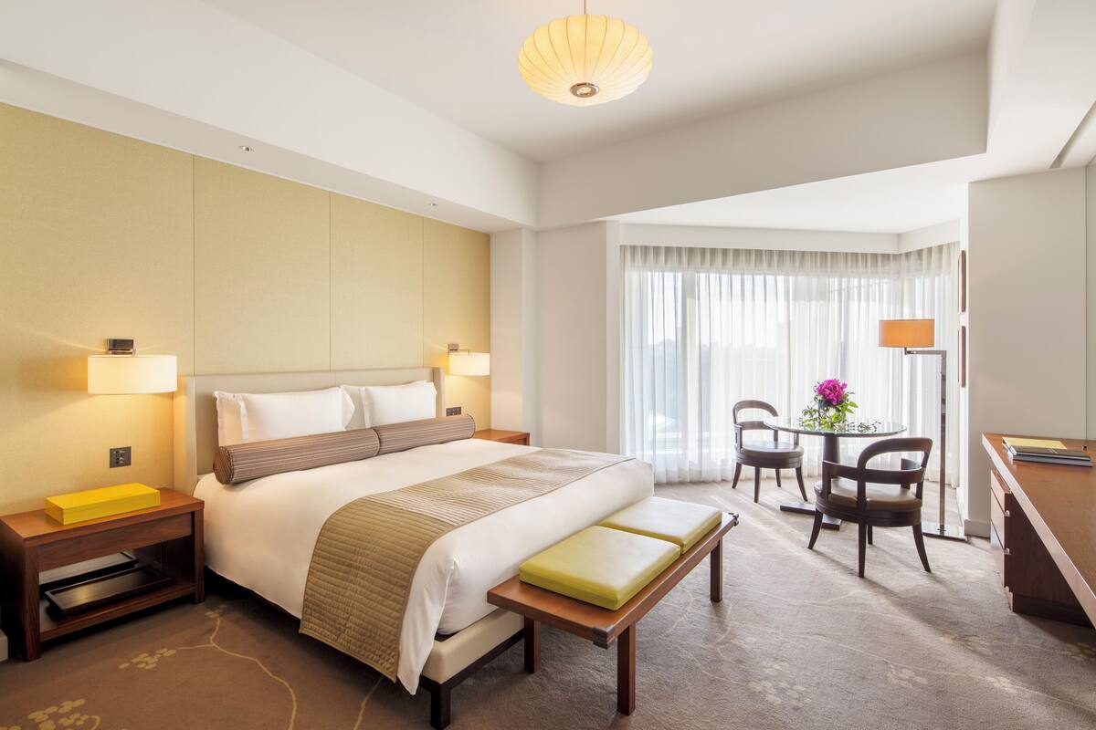 A hotel room with a large bed, bedside tables, a desk, a chair, and a window with curtains.