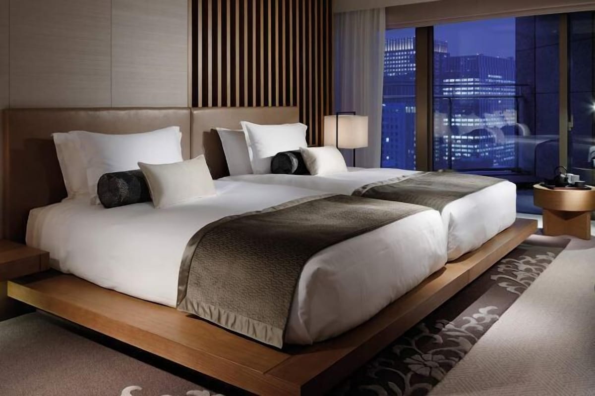 A modern hotel room with a large bed, a nightstand, and a view of the cityscape.