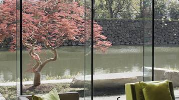 A modern interior with a glass table, green sofa, and a view of a pond with red foliage.