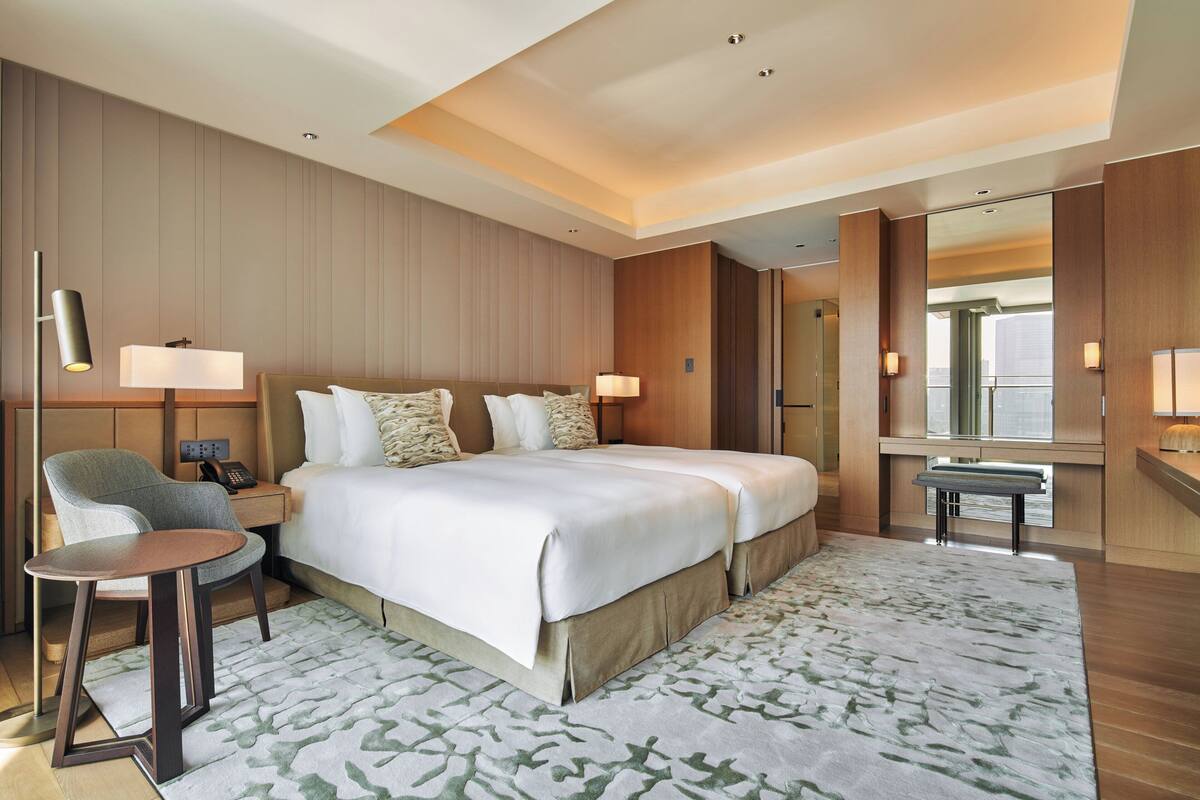 A hotel room with a large bed, bedside tables, a chair, a desk, and a mirror.