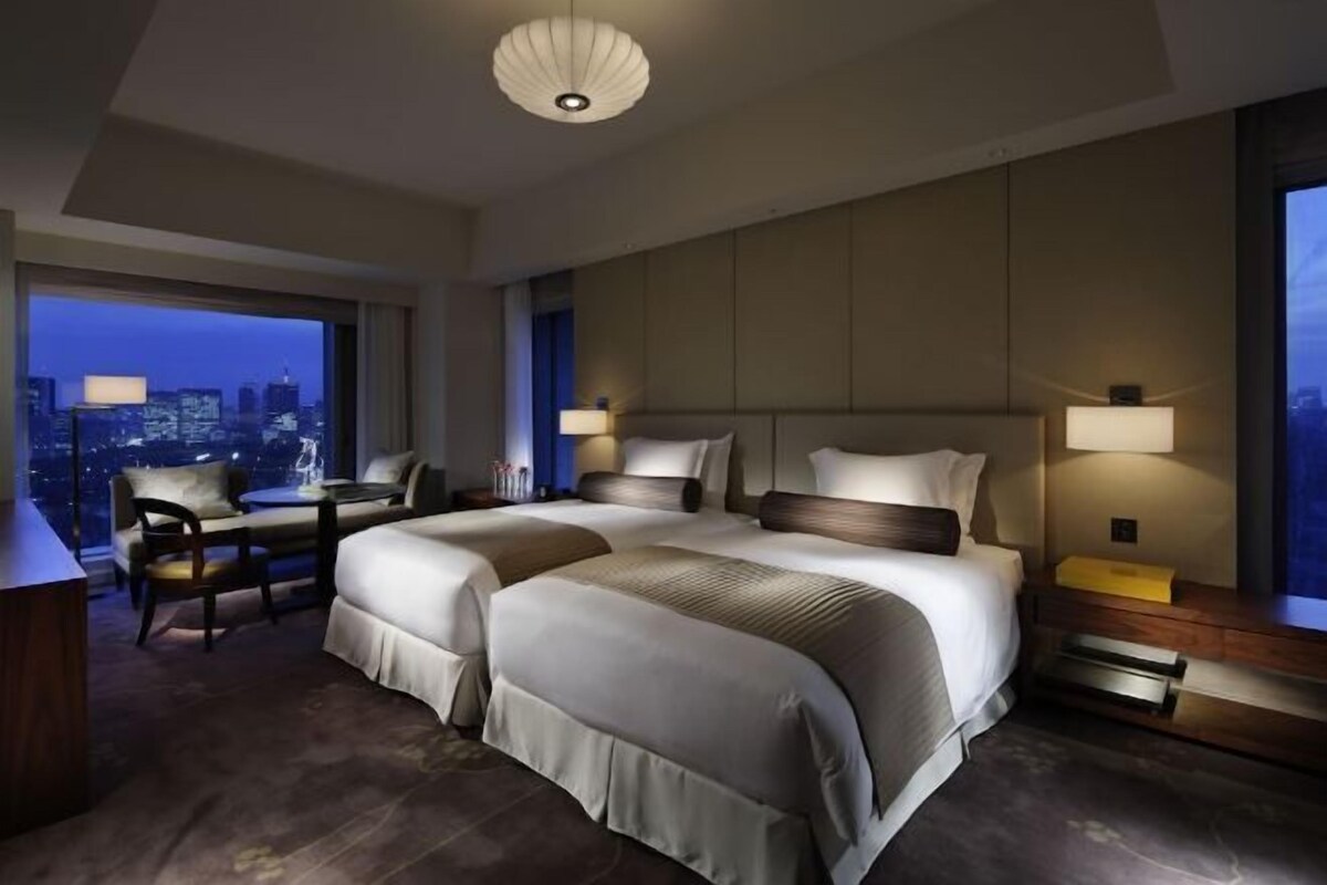 A modern hotel room with a large bed, a desk, and a view of the cityscape.