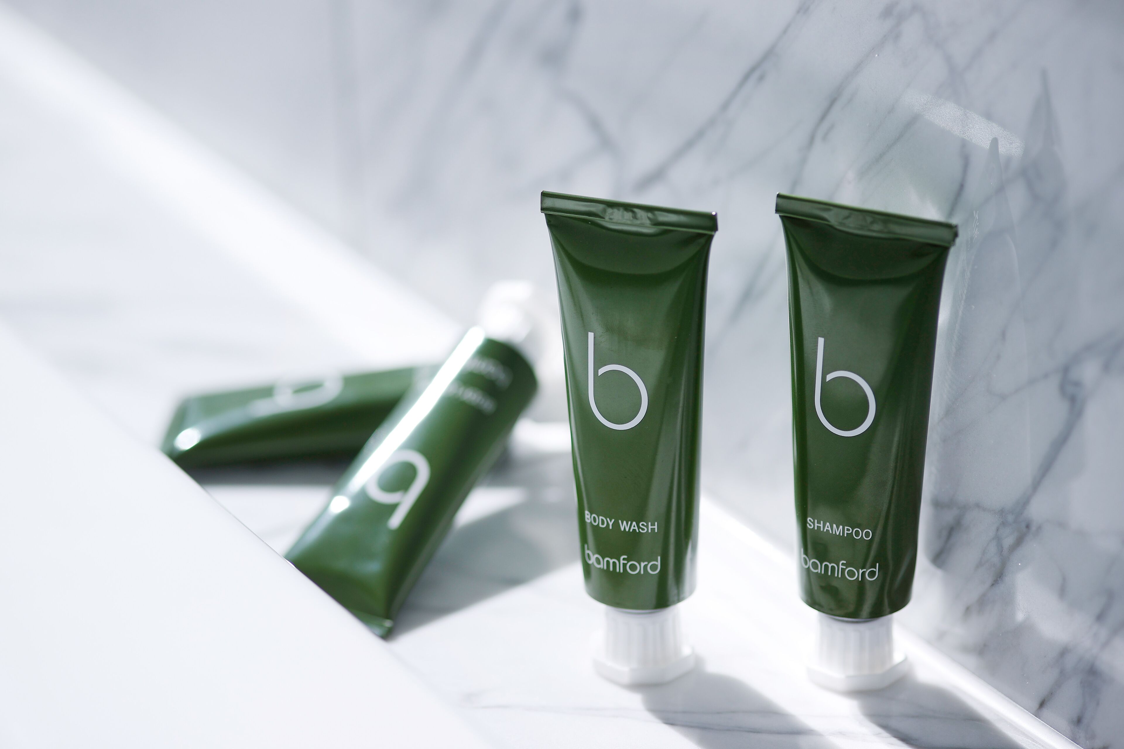 Two green tubes of body wash and shampoo labeled 'b' on a marble surface.