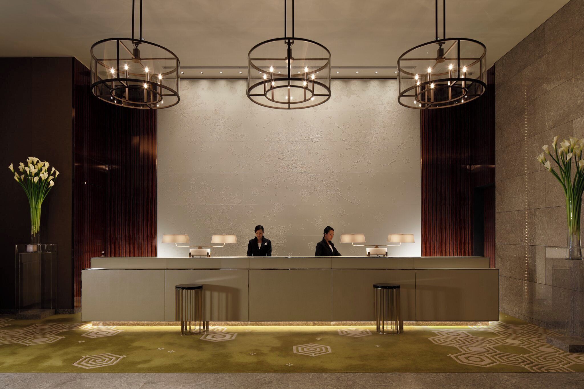 A reception desk with three pendant lights, a reception area with two staff members, and patterned carpet.