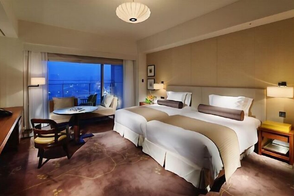 A hotel room with a large bed, a desk, a chair, and a view of the city.