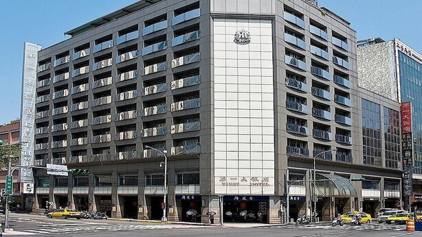 A multi-story hotel with a prominent sign on the facade, multiple balconies, and a clear view of the street below. - First Hotel (Taipei)