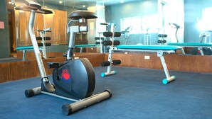 A gym with exercise equipment, including an elliptical and a rowing machine, and a mirrored wall reflecting the equipment. - First Hotel (Taipei)