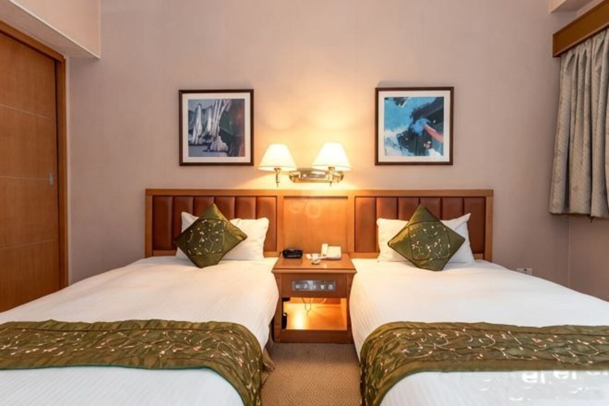 A hotel room with two beds, a wooden headboard, bedside tables with lamps, and framed pictures on the wall.