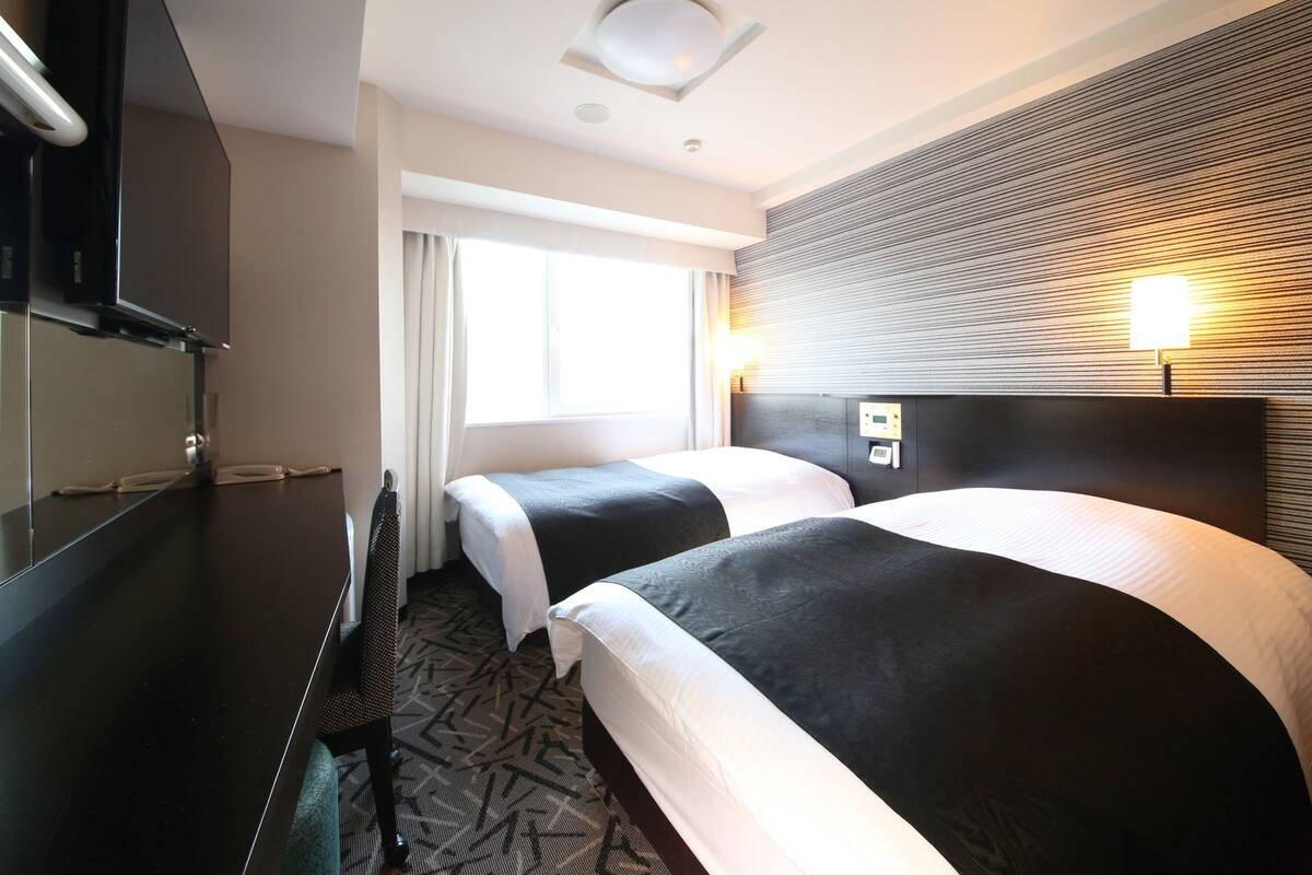 Ett hotellrum med två sängar, en platt-TV, ett skrivbord och ett fönster med gardiner.