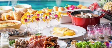 A buffet with various dishes, including meats, fruits, and desserts, set up by a pool.