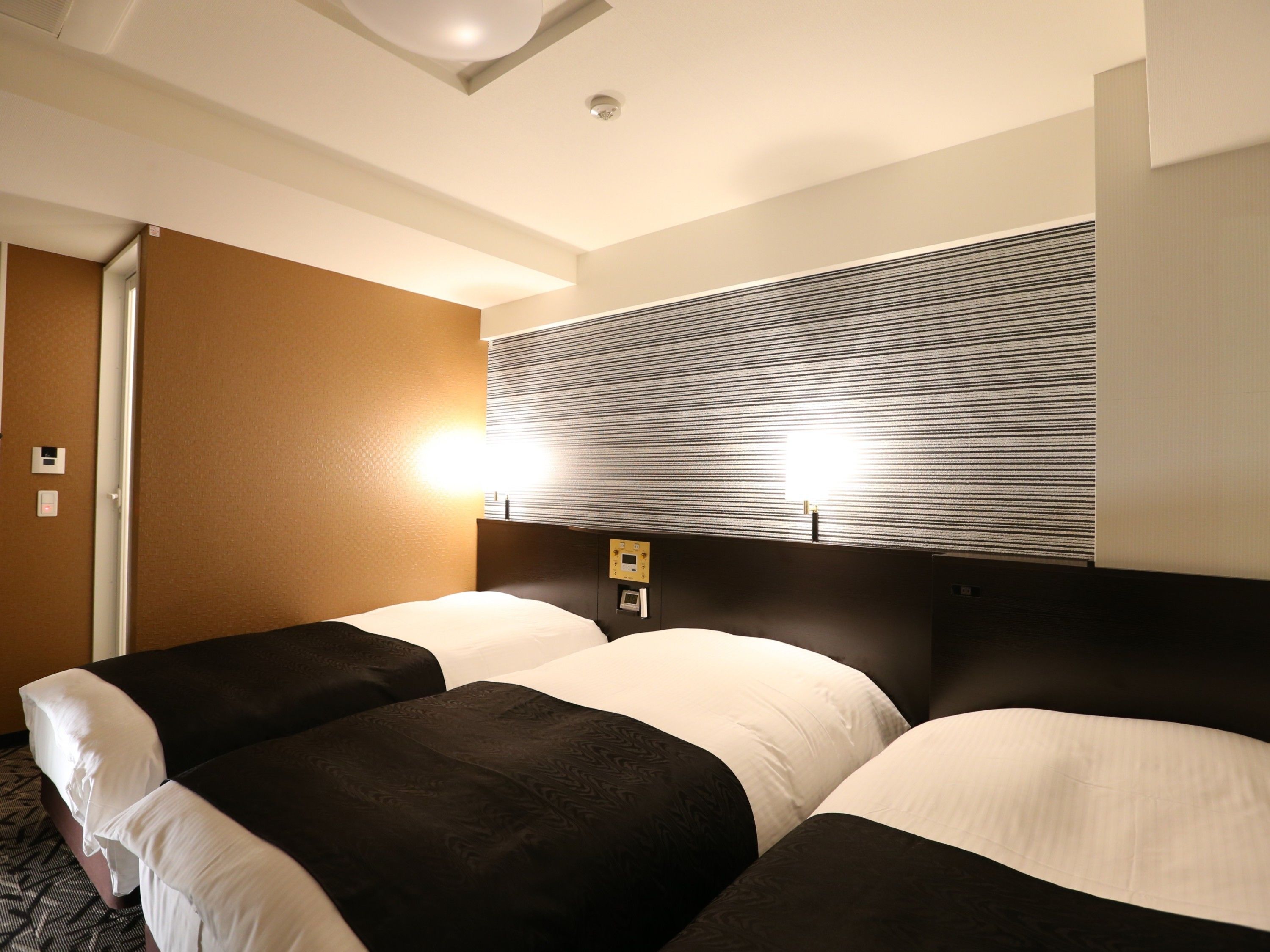 A hotel room with a large bed, a headboard with a light fixture, and a wall with a striped pattern.