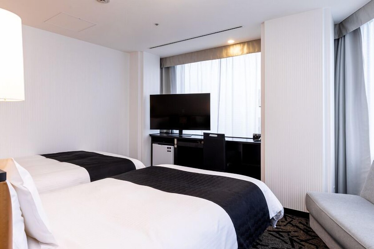 A hotel room with two beds, a desk with a television, and a sofa.