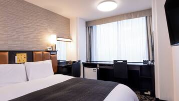 A hotel room with a large bed, a desk, a chair, a flat-screen TV, and a window with curtains.