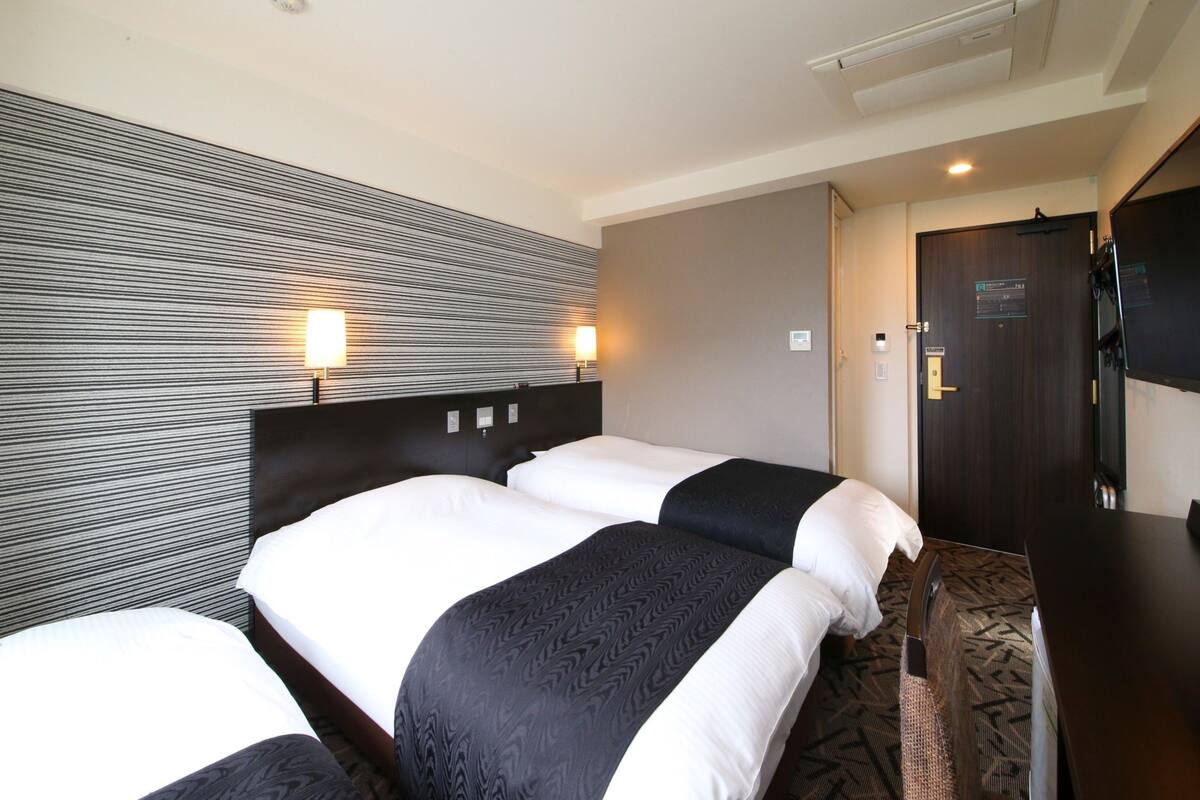 Ett hotellrum med två sängar, en mörk träfärgad sänggavel, en randig vägg och en dörr med en skylt.