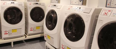 A row of white front-loading washing machines with control panels and safety instructions.